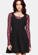 Woman wearing a black mini dress with purple lace long sleeved top underneath on a white background