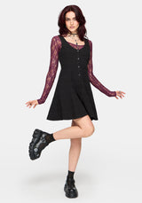 Woman wearing a black dress with a purple long sleeved top underneath, against a white background