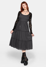 Woman wearing a grey midi dress over a black lace long sleeve top on a white studio background