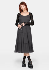 Woman wearing a grey midi dress over a black lace long sleeve top on a white studio background