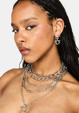 A close-up of a model wearing layered silver chain necklaces, a matching silver nose ring, and a silver hoop earring with a stylized 'U' charm.