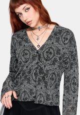 Woman wearing a black patterned v-neckline cardigan over a black outfit on a white background