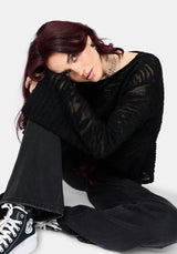 Woman wearing a black distressed jumper with long sleeves and back denim jeans on a white background