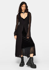A model wearing a black long-sleeve lace-trimmed cardigan over a black velvet midi dress, styled with black combat boots and a choker, against a light gray studio background.