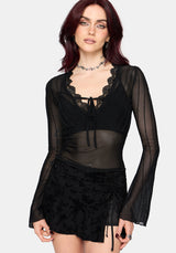 Woman wearing a black lace mesh top with long sleeves on a plain background