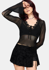 Woman wearing a black lace mesh top with long sleeves on a plain background