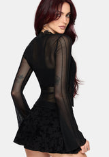 Woman wearing a black lace mesh top with long sleeves on a plain background