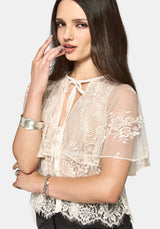 Woman wearing a cream lace blouse with floral lace sleeves on a white background
