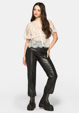 Woman wearing a cream lace top and black leather pants on a white background