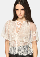 Woman wearing a cream lace top against a plain background