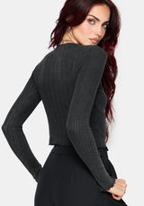 A woman wearing a dark charcoal gray ribbed long-sleeve knit top, shown from a three-quarter back angle against a light gray studio background.