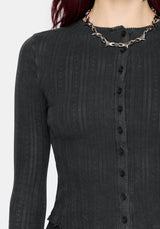 A woman wearing a dark charcoal gray ribbed long-sleeve cardigan with a button-front detail and scalloped hem, styled with a chunky silver chain necklace against a light gray background.