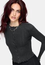 A woman wearing a dark charcoal gray ribbed long-sleeve cardigan with a button-front detail and scalloped hem, styled with a chunky silver chain necklace against a light gray background.