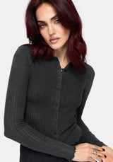 A woman with dark red hair wearing a dark charcoal gray ribbed long-sleeve button-up knit top, photographed against a light gray studio background.