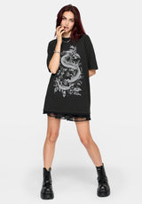 A model with dark red hair wearing an oversized black t-shirt dress featuring a large white dragon graphic on the front, styled with black lace-up combat boots against a light gray background.