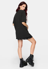 A woman modeling an oversized black t-shirt with a large white graphic print of a coiled snake and floral elements on the front, set against a plain light gray background.