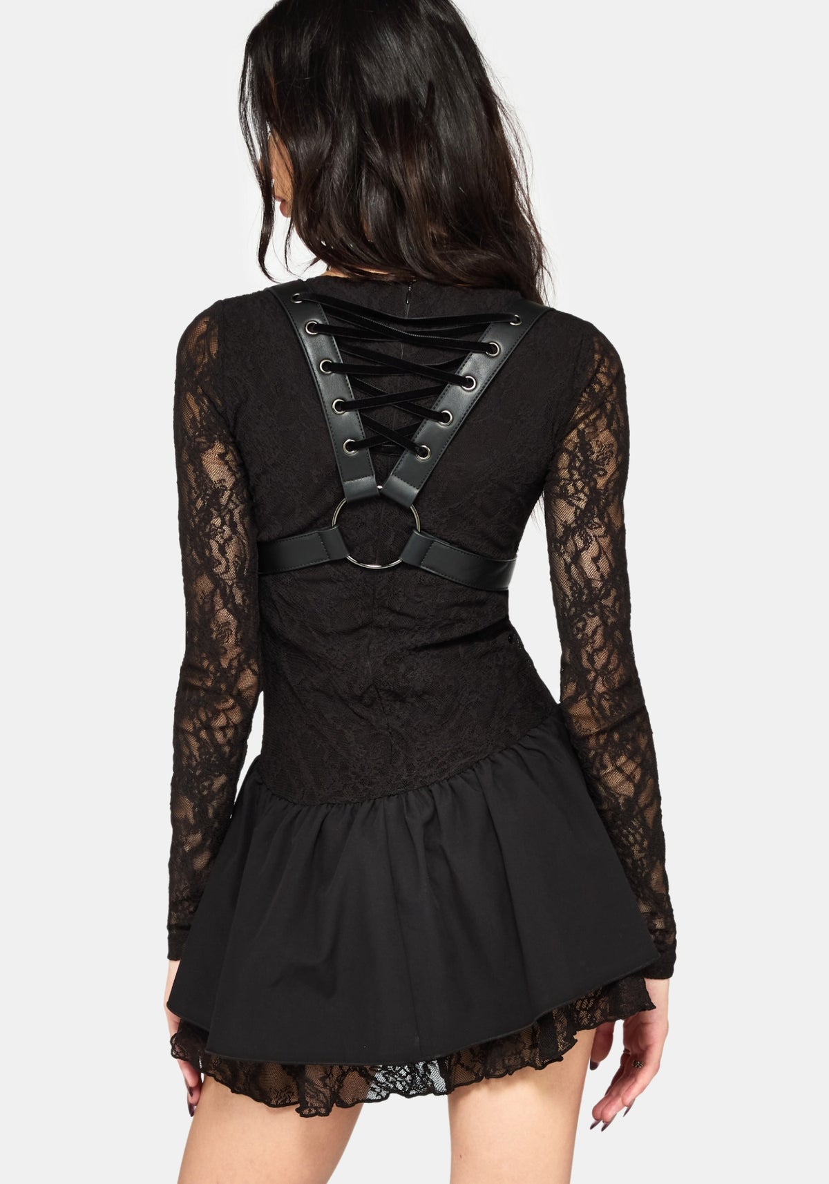 A woman shown from the back wearing a black lace long-sleeve mini dress with a lace-up harness-style back detail and a ruffled skirt, against a light gray studio background.