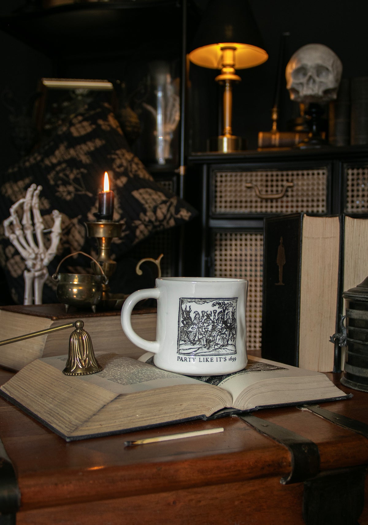 Mug with a design on a wooden surface with books and candles in a darkly decorated room.