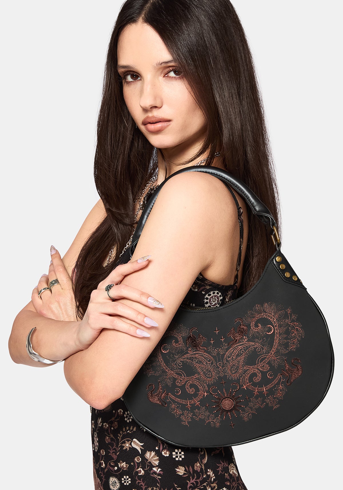 Woman holding a black handbag with intricate designs on a plain background