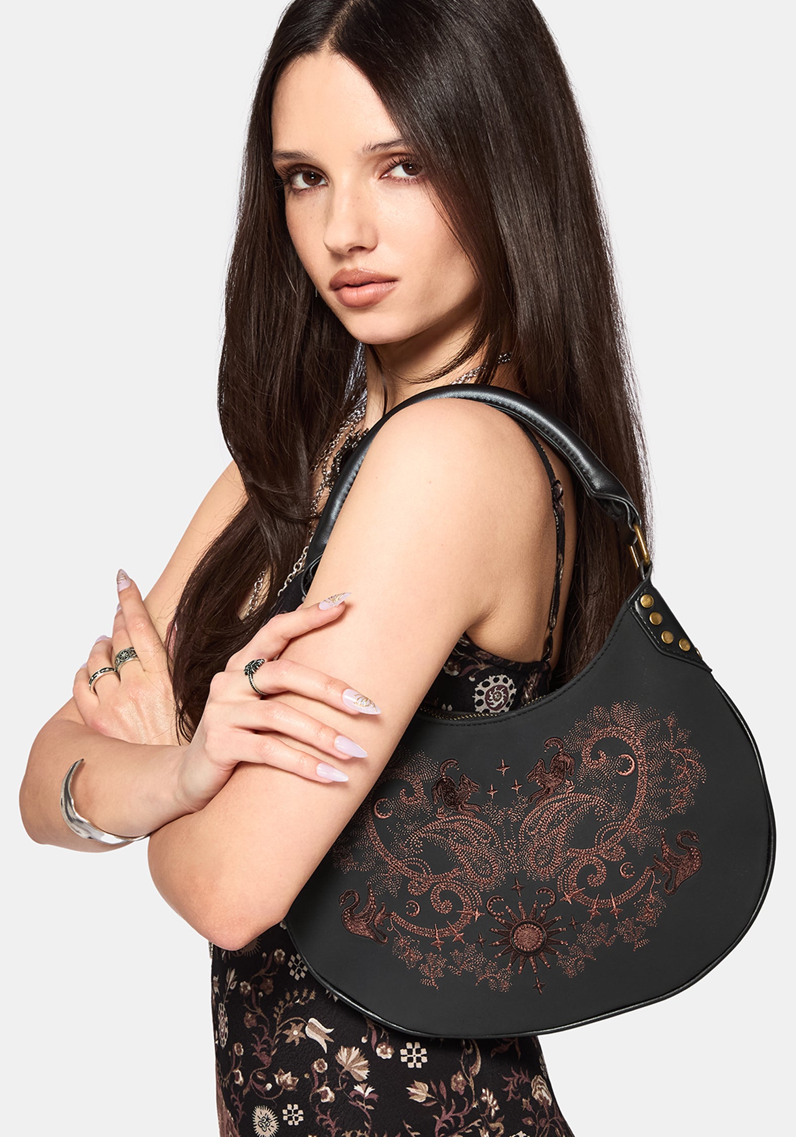 Woman holding a black handbag with intricate designs on a plain background