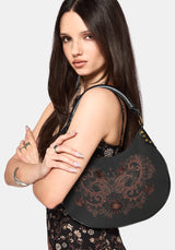 Woman holding a black handbag with intricate designs on a plain background