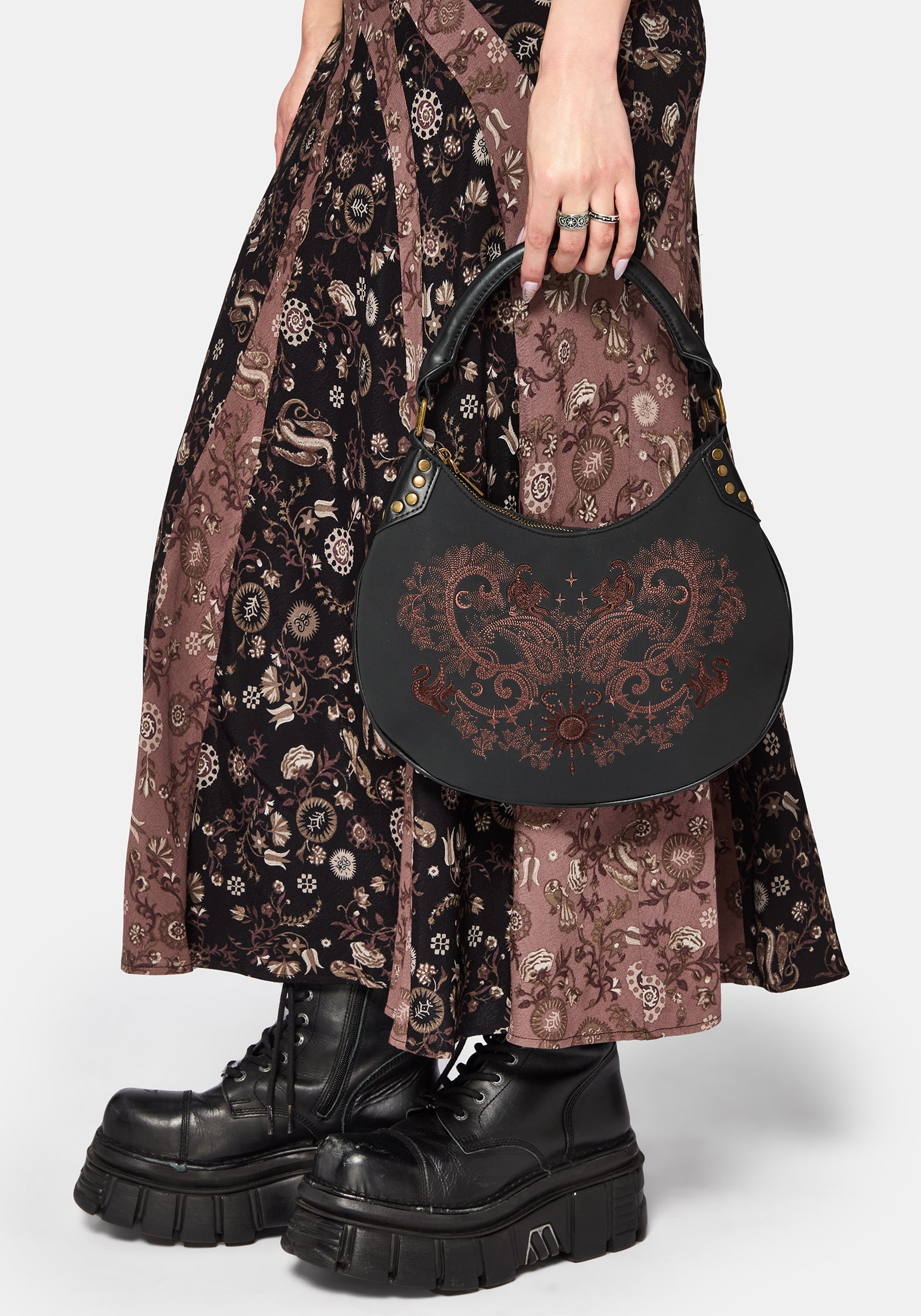 Person wearing a patterned dress and holding a black handbag with intricate design.