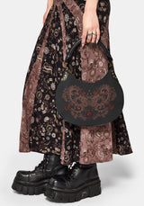 Person wearing a patterned dress and holding a black handbag with intricate design.