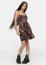 A woman modeling a sleeveless mini dress with a bohemian paisley pattern in black, rust red, and beige, paired with black combat boots against a light gray studio background.