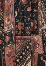 A close-up of a patterned textile with mixed panels in dusty pink, rust red, black, and beige, featuring floral, sunburst, and geometric motifs.