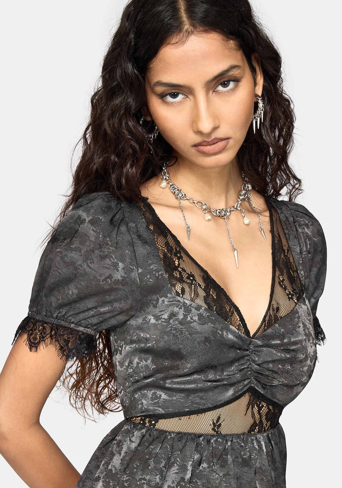 A woman modeling a dark gray and black patterned dress with lace trim, sheer mesh panels, and puff sleeves against a light gray background.