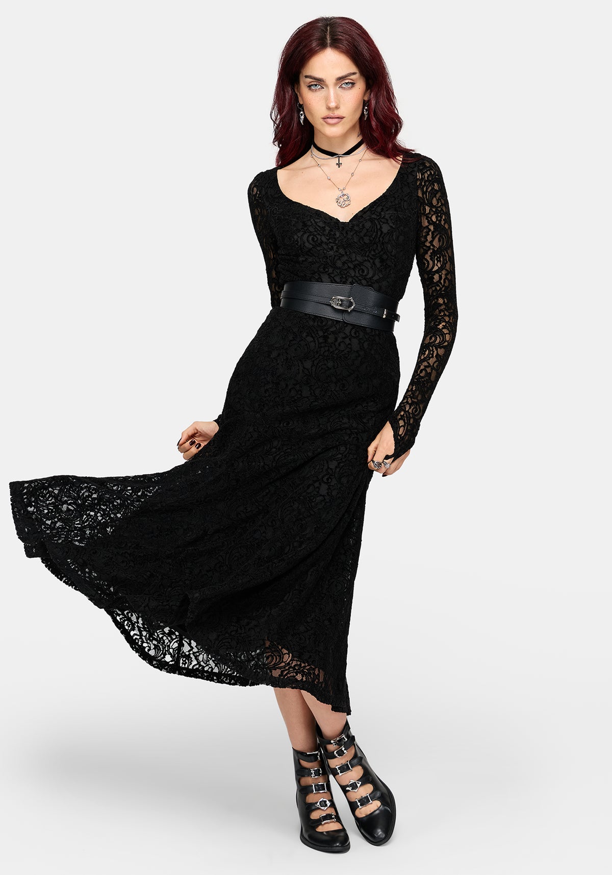 A woman modeling a black lace long-sleeve maxi dress with a wide black belt at the waist, paired with black lace-up ankle boots, against a light gray studio background.