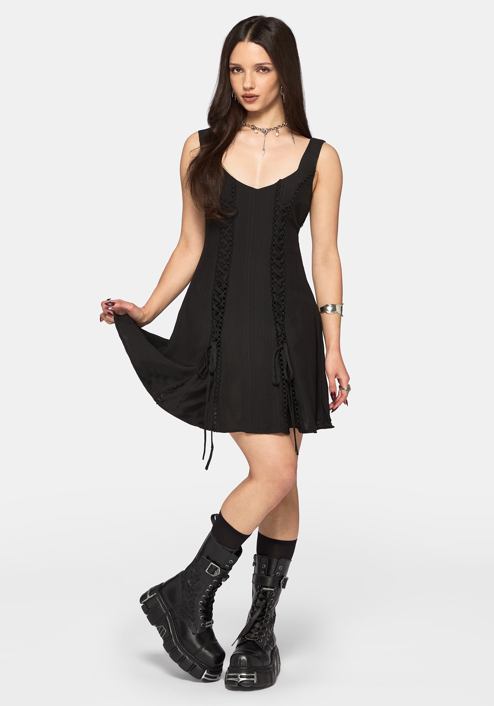 Woman wearing a black dress with lace-up front and black boots on a white background