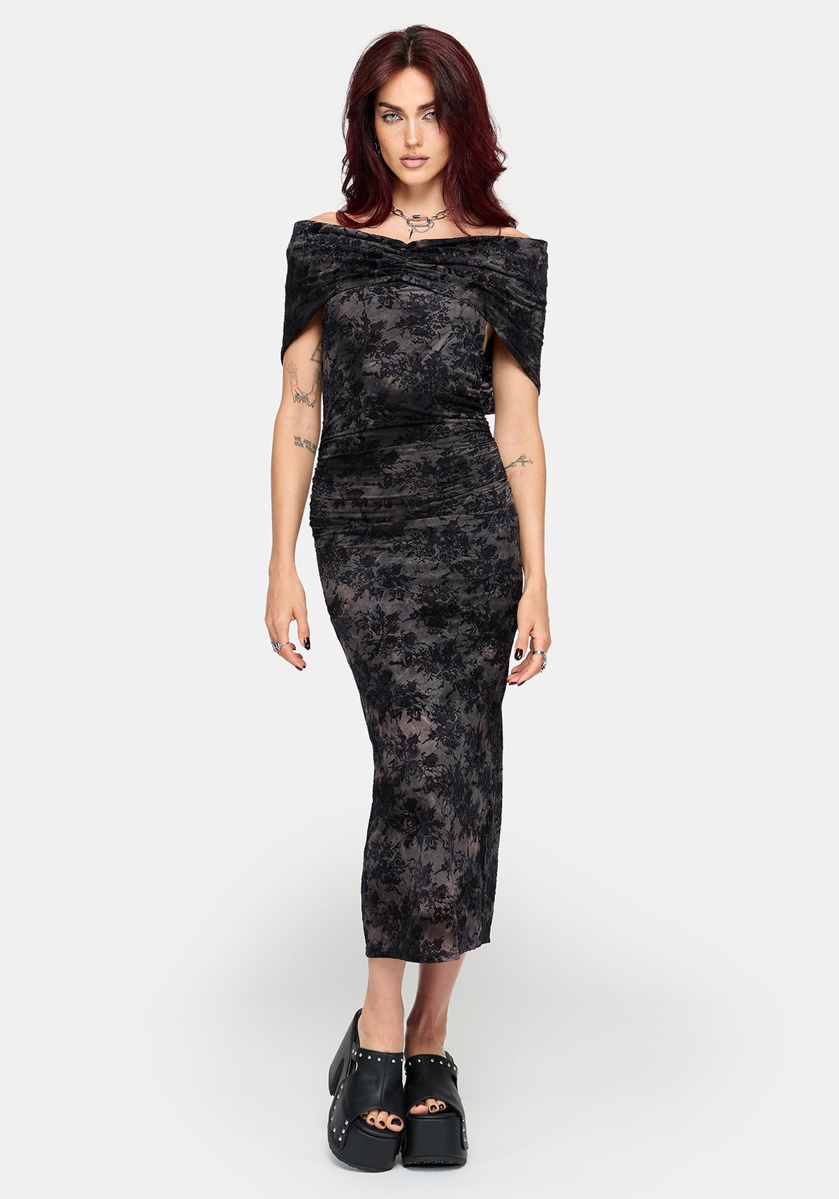 A woman modeling an off-the-shoulder patterned midi dress with a textured, slightly sheer floral lace-like pattern, paired with black platform shoes, against a light gray studio background.