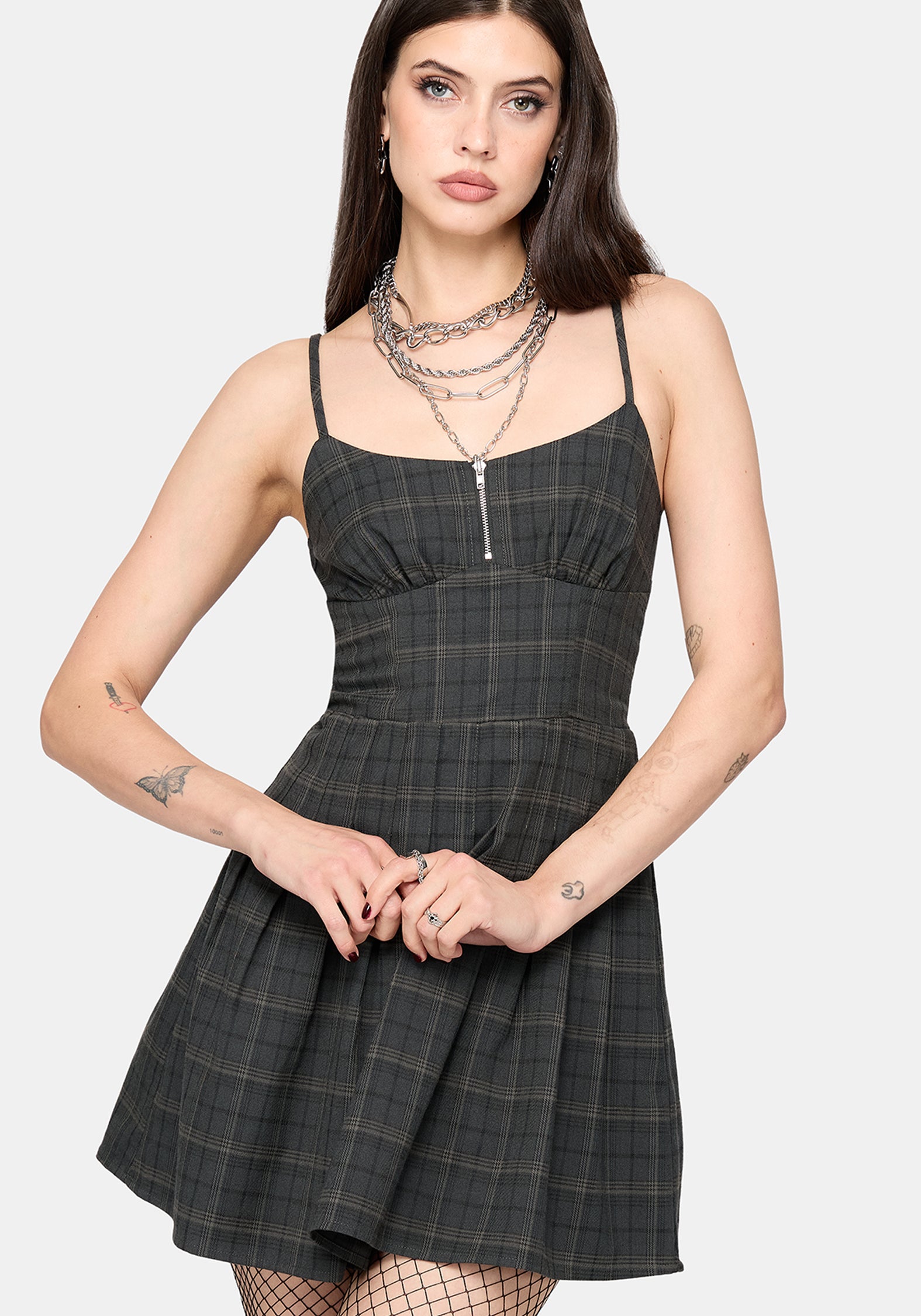A woman modeling a dark gray plaid mini dress with thin straps, a square neckline, and a flared skirt, styled with layered silver chain necklaces against a light gray background.