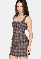 A woman modeling a sleeveless mini dress with a red, gray, and white plaid pattern, featuring a button-down front and a self-tie waist belt, set against a plain light gray background.