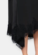 Close-up of a black dress with a sheer overlay and floral lace trim along the hem, shown on a model against a light gray background.