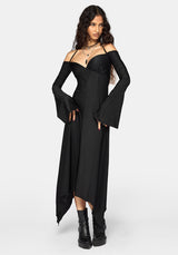 A woman modeling a black off-the-shoulder maxi dress with dramatic bell sleeves and an asymmetrical hem, paired with black platform ankle boots against a light gray studio background.