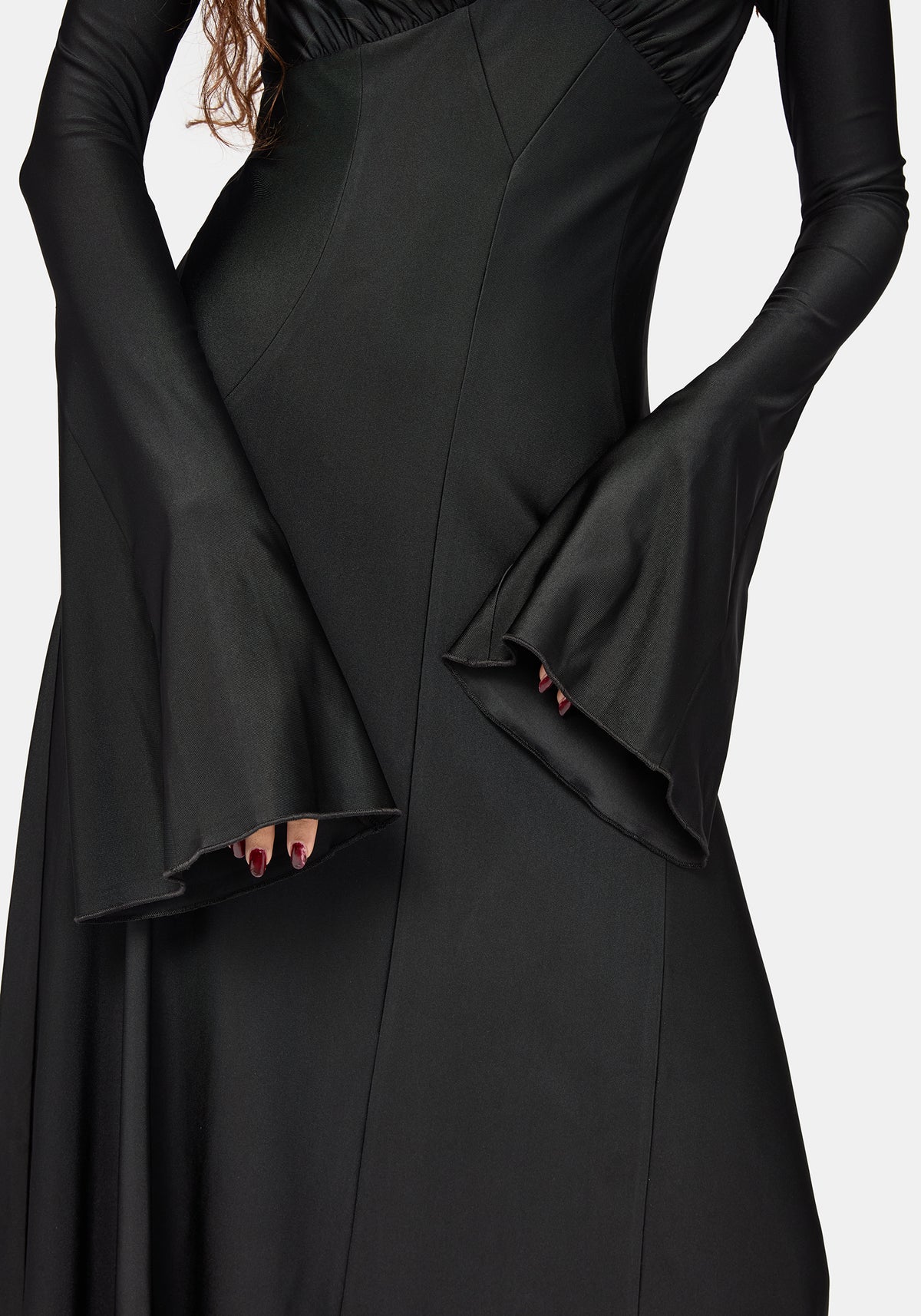 A close-up of a black long-sleeve midaxi dress with dramatic flared bell sleeves and structured seams, shown on a model against a light gray background.