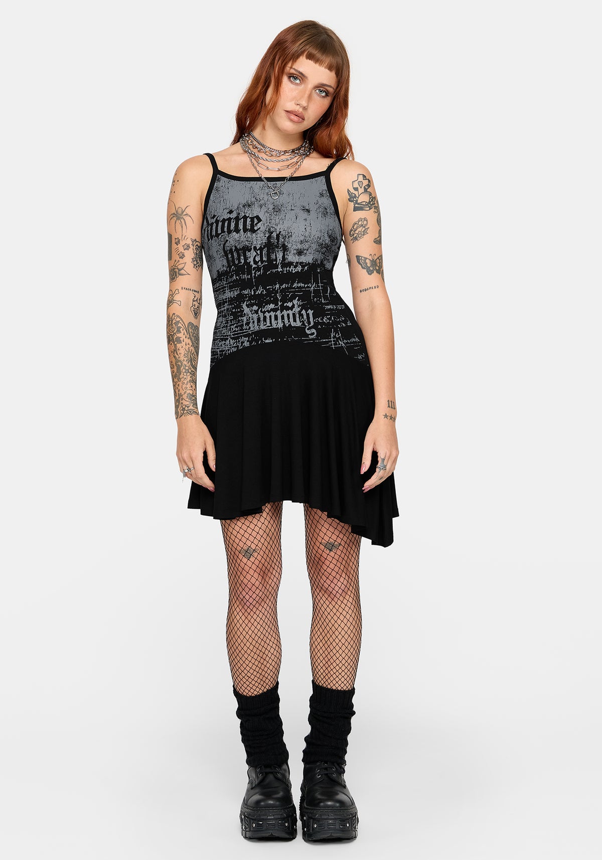 A model wearing a black and grey graphic mini dress, styled with fishnet tights, black socks, and black platform boots against a light gray background.