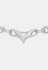 A close-up of a polished silver chain necklace featuring a distinctive central triangular clasp with looped details, set against a solid light gray background.