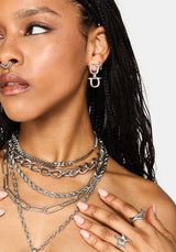 A close-up of a model wearing layered silver chain necklaces, a matching silver hoop earring with a stylized letter 'H' design, and silver star-shaped rings on her fingers.