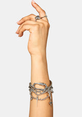 A close-up of a person's hand and wrist wearing multiple layered silver-tone chain bracelets and rings against a light gray background.