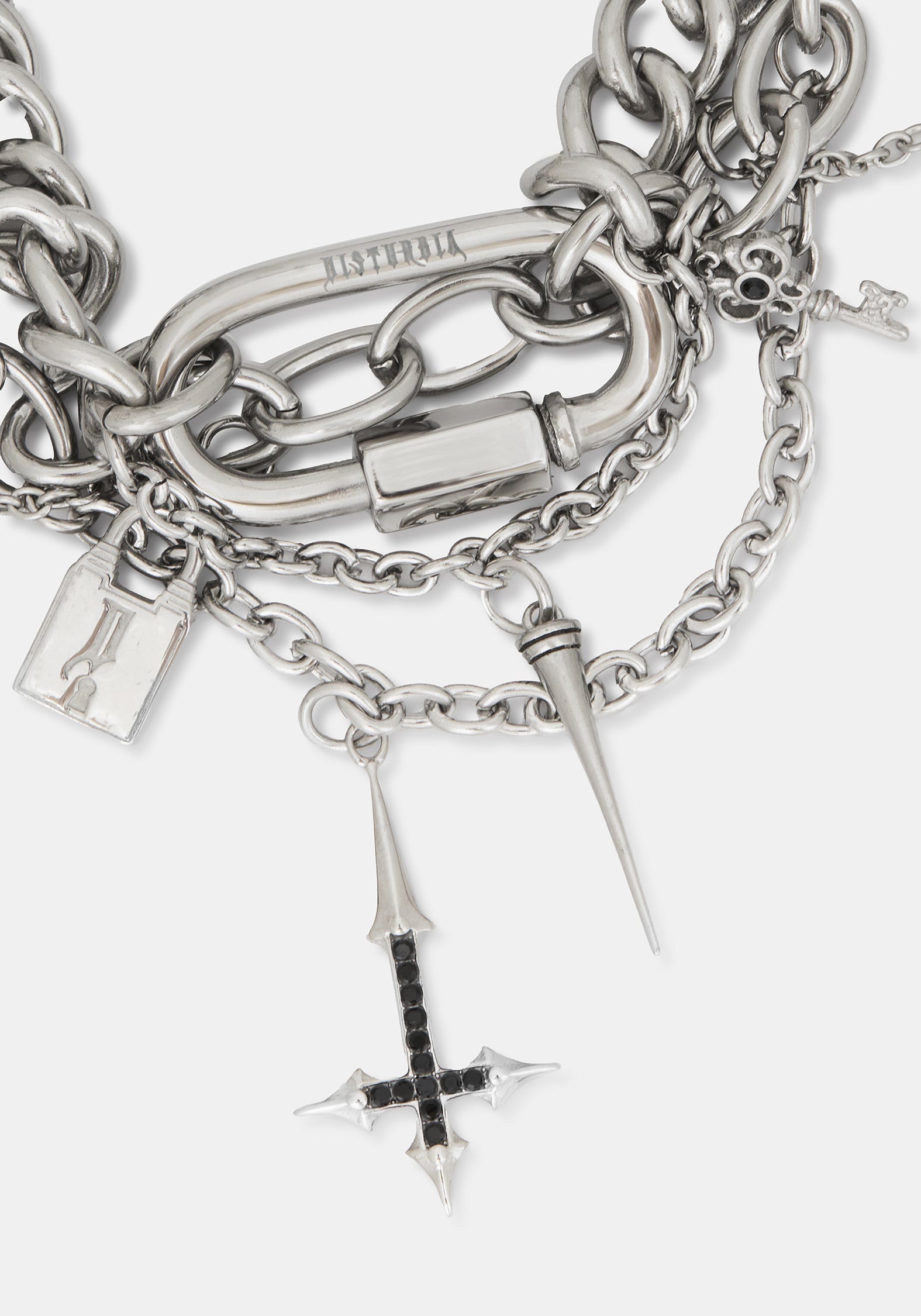 A close-up of a chunky silver chain bracelet with multiple charms, including a padlock, spikes, a skull, and a cross charm with black accents. 