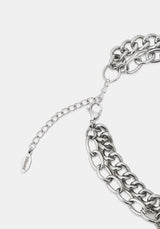 Close-up of a silver-toned chunky chain necklace with an adjustable extender chain and a small branded tag, photographed on a light gray background.