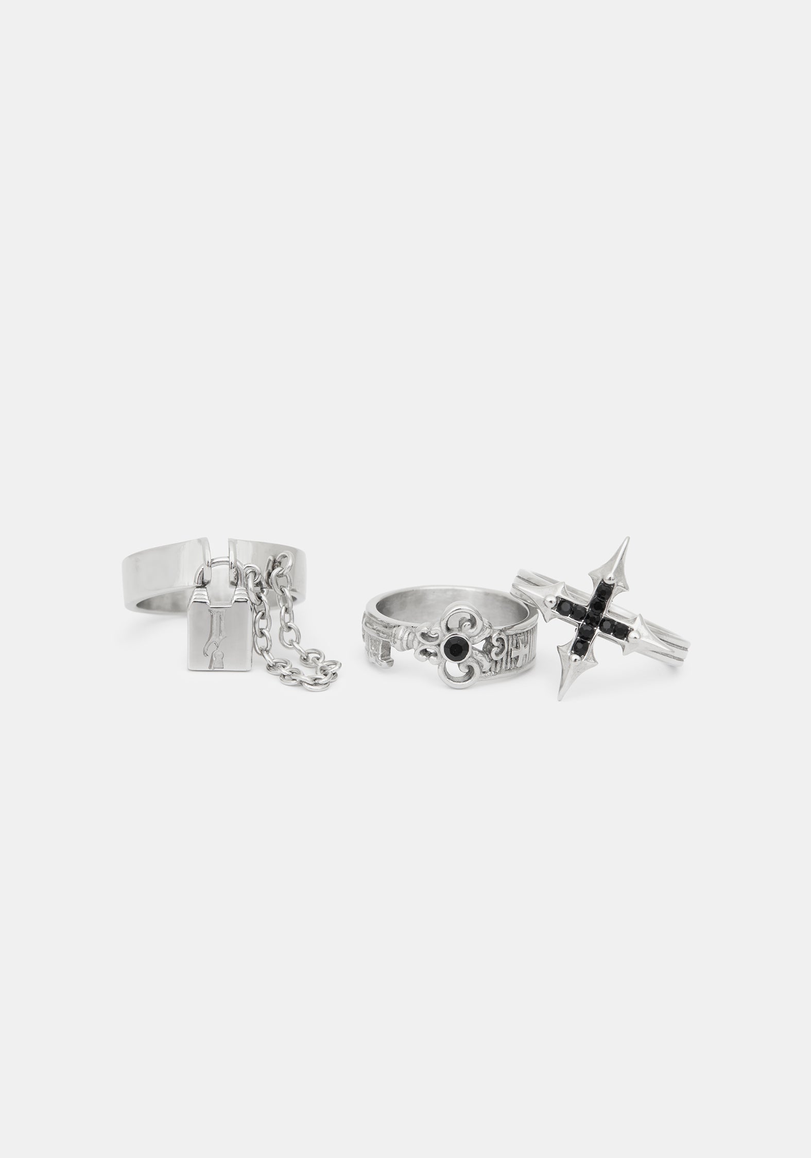 Three silver-toned gothic-style rings displayed on a light gray background, including a cross ring with black accents, a ring with a hanging chain and padlock charm, and a ring with a skull detail.
