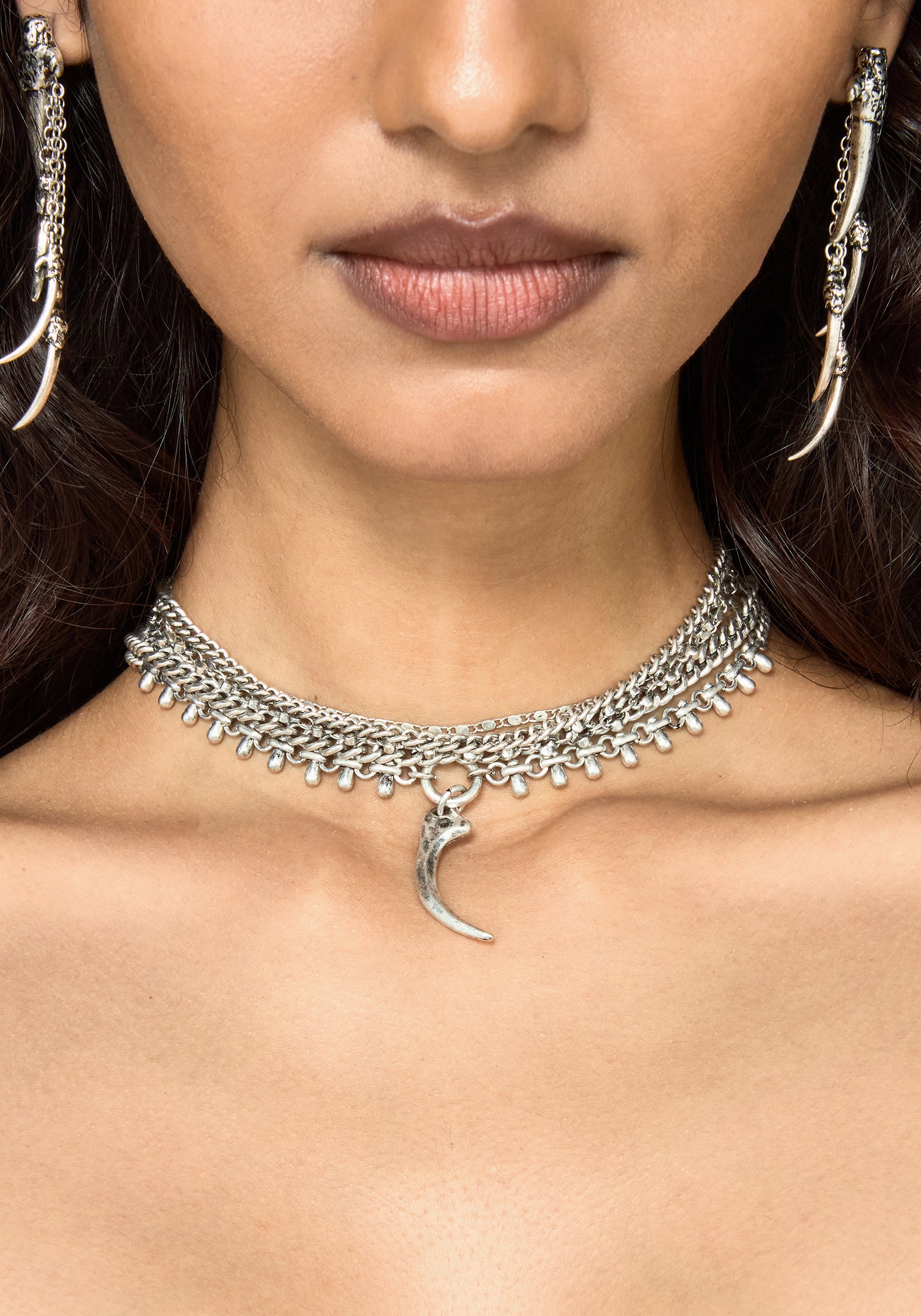 A close-up of a model wearing a silver-toned chain choker necklace with a crescent moon pendant, along with matching long dangling earrings.