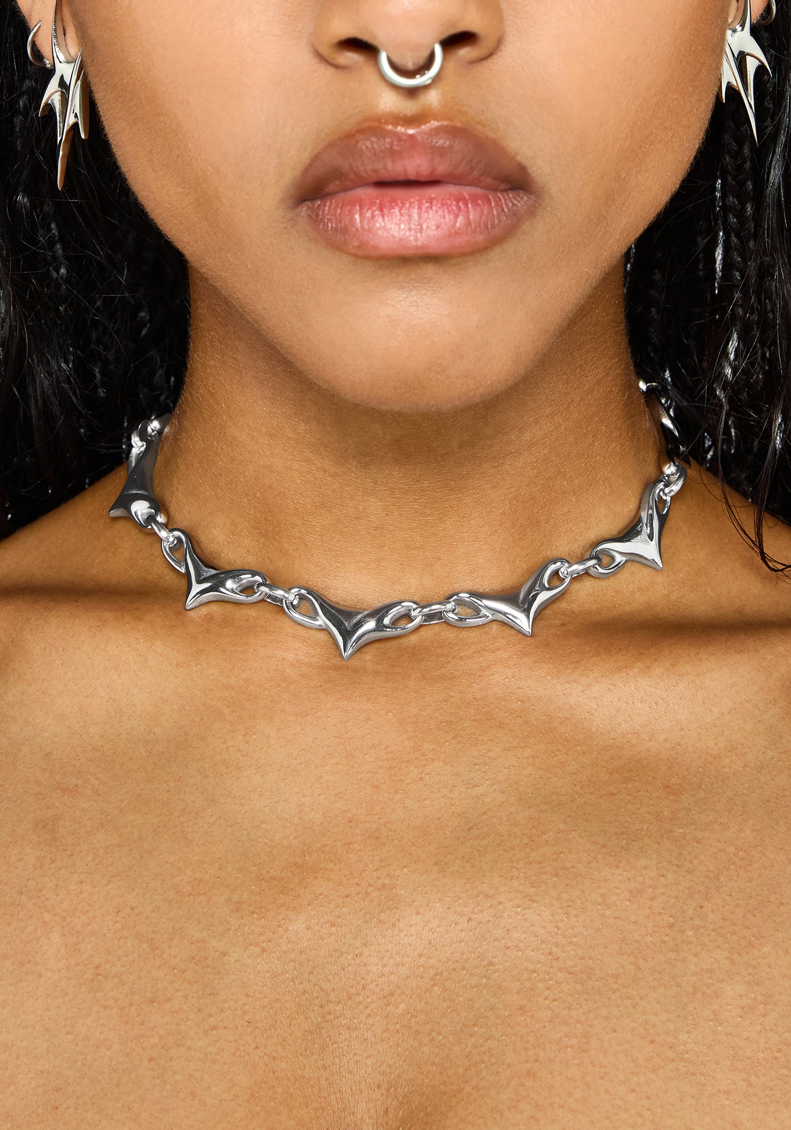 A close-up of a model wearing a silver gothic-style chain choker necklace with sharp, pointed bat-wing-like links.