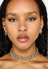 A close-up of a model wearing a chunky silver chain choker, along with matching silver hoop earrings and a nose ring, against a plain white background.