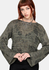 Woman wearing a patterned green jumper and black pants against a plain background