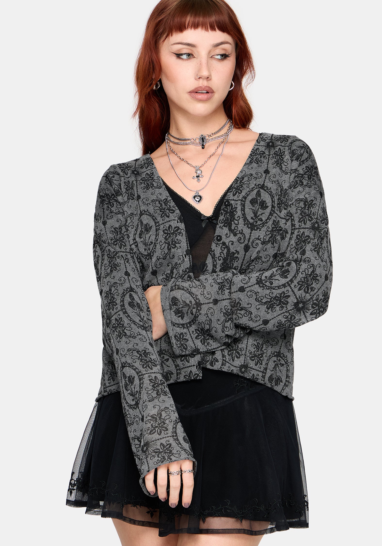 Woman wearing a black patterned cardigan over a black top and skirt on a white background